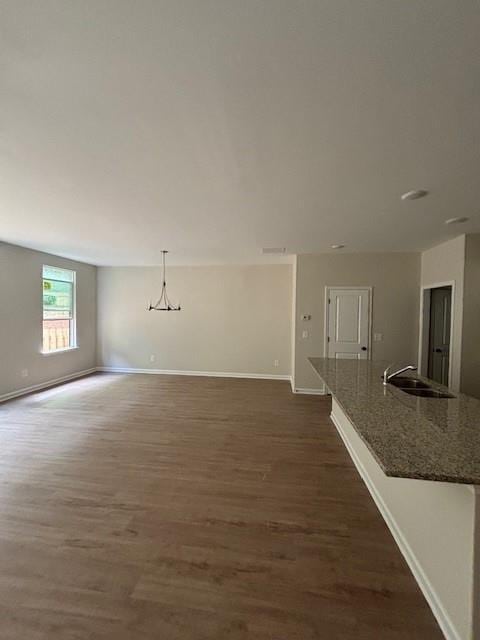 unfurnished living room featuring sink, dark wood-type flooring, and a notable chandelier