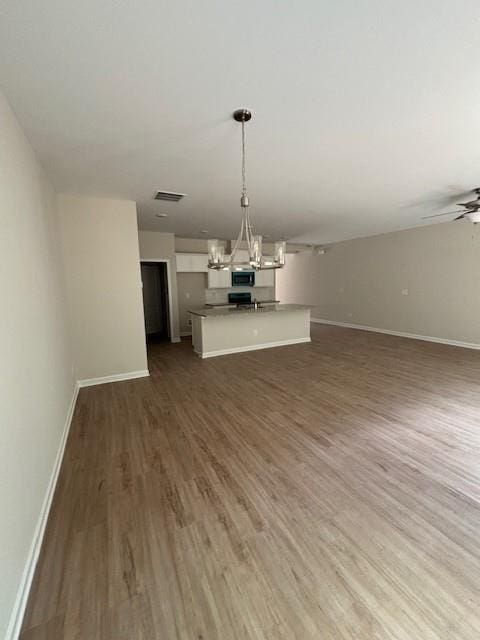 unfurnished living room featuring ceiling fan with notable chandelier and dark wood-type flooring