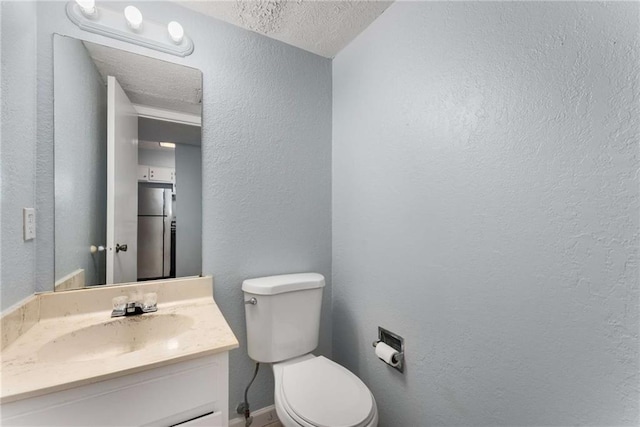 bathroom featuring a textured ceiling, a textured wall, toilet, vanity, and baseboards