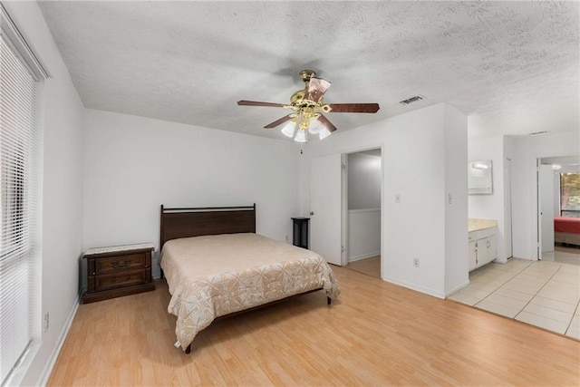 bedroom featuring light wood-type flooring, a textured ceiling, baseboards, and ensuite bathroom