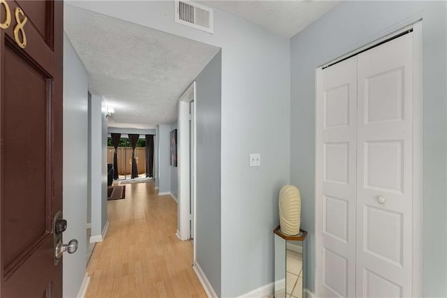 hall with a textured ceiling, light wood finished floors, and baseboards