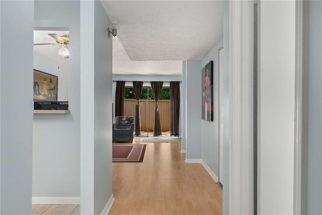 hallway featuring a textured ceiling, baseboards, and wood finished floors
