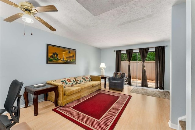 living area featuring wood finished floors, a textured ceiling, baseboards, and a ceiling fan