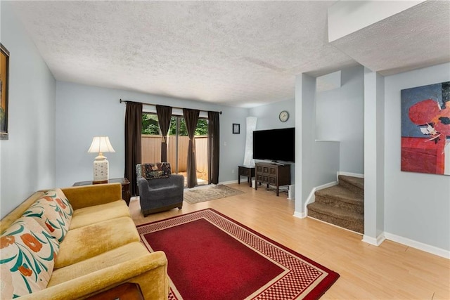 living room with wood finished floors, a textured ceiling, stairway, and baseboards