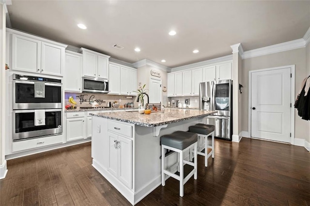 kitchen with a kitchen island with sink, white cabinets, light stone countertops, and appliances with stainless steel finishes