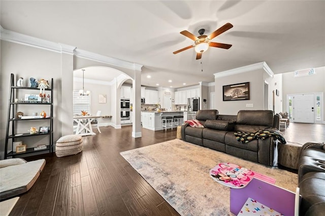 living room featuring ceiling fan with notable chandelier, crown molding, and dark wood-type flooring