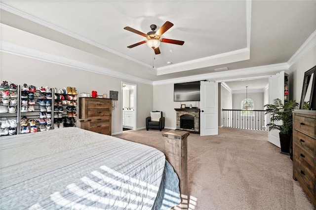 carpeted bedroom with ensuite bathroom, ornamental molding, a raised ceiling, ceiling fan, and a stone fireplace