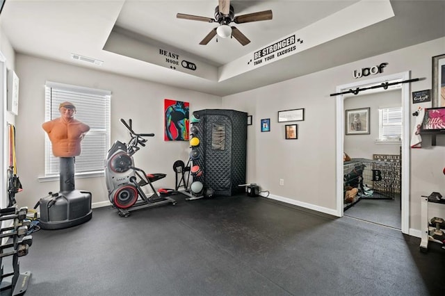 exercise area with ceiling fan, a healthy amount of sunlight, and a raised ceiling