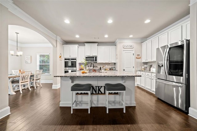 kitchen featuring white cabinets, stainless steel appliances, light stone counters, and a kitchen island with sink