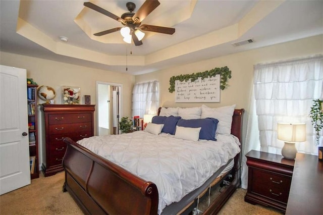 carpeted bedroom featuring ceiling fan and a tray ceiling