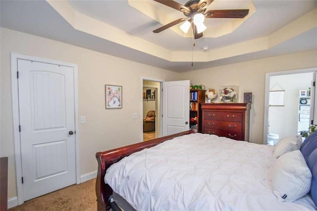 carpeted bedroom with ensuite bath, a raised ceiling, and ceiling fan