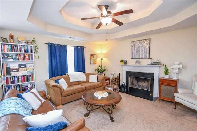 carpeted living room with a raised ceiling and ceiling fan