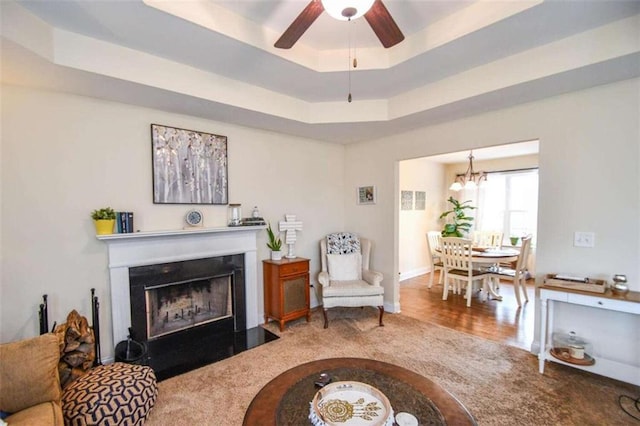 living room featuring carpet, ceiling fan with notable chandelier, and a tray ceiling