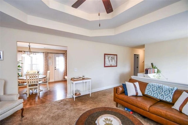 carpeted living room featuring a raised ceiling and ceiling fan with notable chandelier