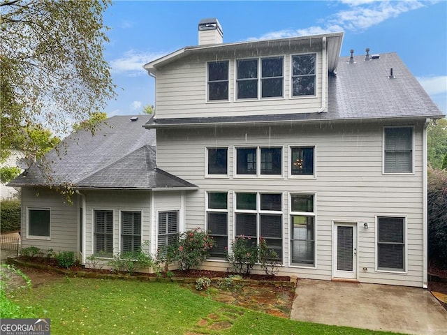 back of property featuring a yard, a shingled roof, a chimney, and a patio area