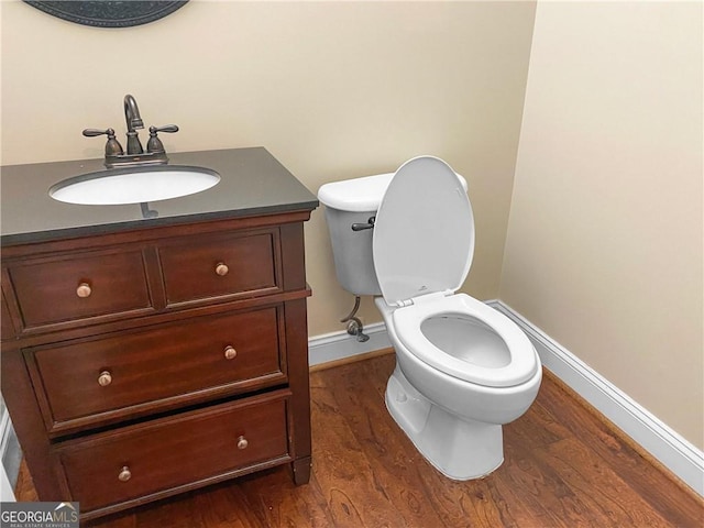 half bath with baseboards, toilet, wood finished floors, and vanity