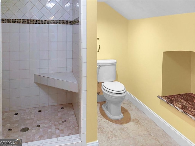 bathroom with tile patterned flooring, tiled shower, toilet, and baseboards