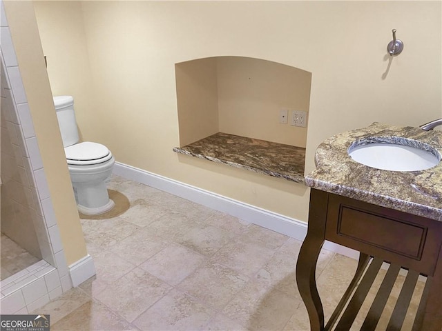 bathroom with tiled shower, baseboards, toilet, and vanity