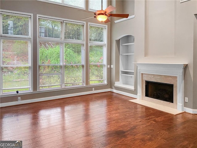 unfurnished living room featuring built in features, wood-type flooring, and a high end fireplace