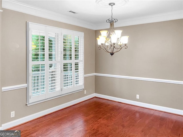 empty room with visible vents, crown molding, baseboards, a chandelier, and wood finished floors