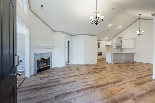 unfurnished living room with a fireplace, visible vents, an inviting chandelier, high vaulted ceiling, and light wood-type flooring