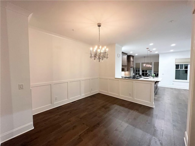 unfurnished dining area with sink, dark hardwood / wood-style flooring, a chandelier, and ornamental molding