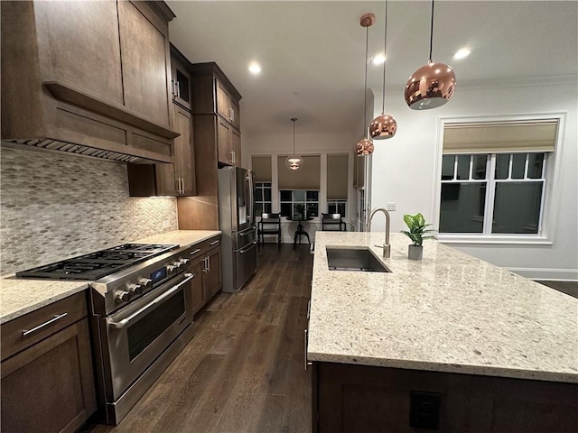 kitchen with a center island with sink, sink, appliances with stainless steel finishes, decorative light fixtures, and dark brown cabinets