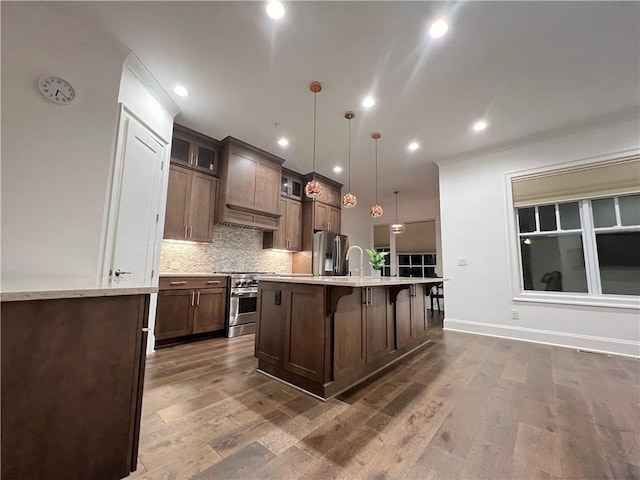 kitchen featuring hanging light fixtures, backsplash, a breakfast bar area, a kitchen island with sink, and appliances with stainless steel finishes