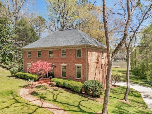 view of front of home with brick siding, a shingled roof, and a front yard