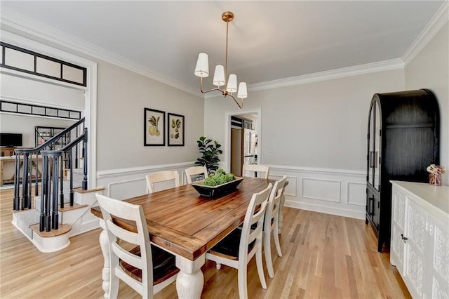 dining area featuring crown molding, light wood-type flooring, a wainscoted wall, stairs, and a decorative wall