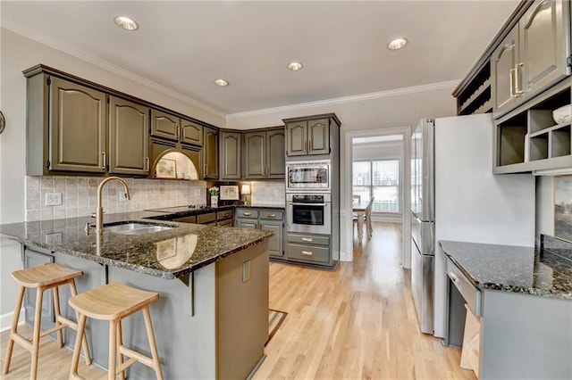 kitchen featuring appliances with stainless steel finishes, a sink, a peninsula, light wood-style flooring, and dark stone counters