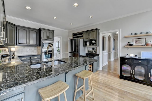 kitchen featuring open shelves, dark stone counters, appliances with stainless steel finishes, a sink, and ornamental molding