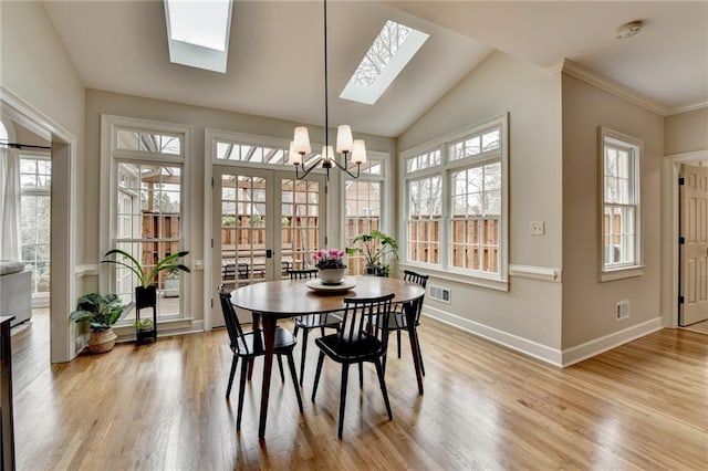 dining room featuring a skylight, baseboards, light wood-style floors, a chandelier, and lofted ceiling