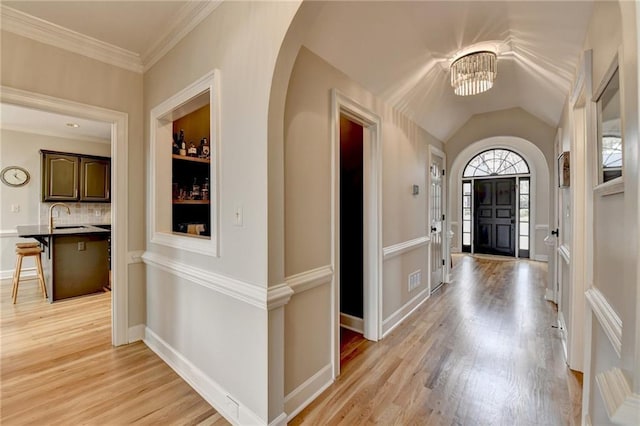 entryway featuring a chandelier, light wood-style floors, arched walkways, and ornamental molding