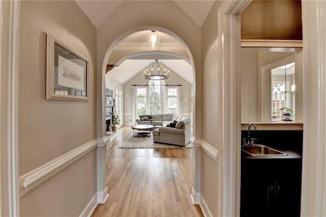 corridor with lofted ceiling, a sink, light wood finished floors, arched walkways, and a chandelier