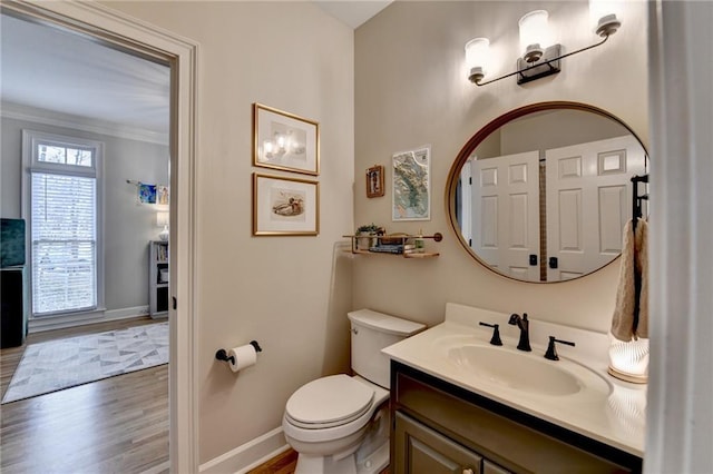 bathroom with baseboards, vanity, toilet, wood finished floors, and crown molding