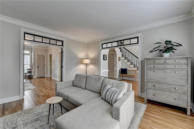 living area with ornamental molding, arched walkways, light wood-style floors, stairway, and baseboards