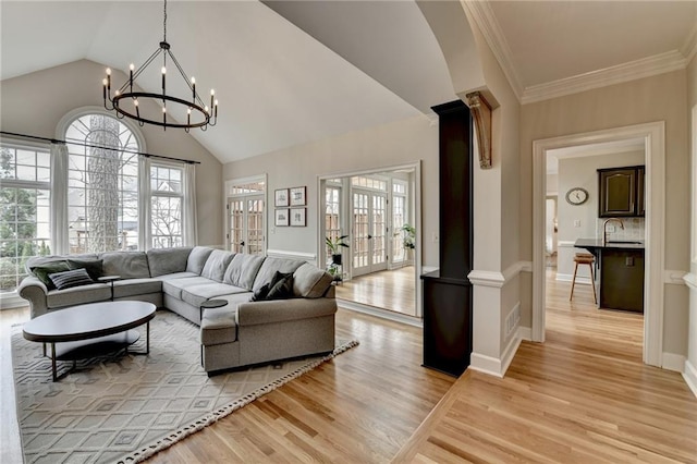 living area featuring a chandelier, light wood-type flooring, lofted ceiling, and ornamental molding
