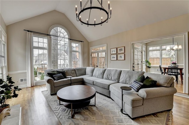 living area with a chandelier, light wood-type flooring, and high vaulted ceiling