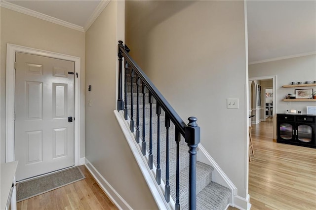 stairs featuring wood finished floors, crown molding, and baseboards