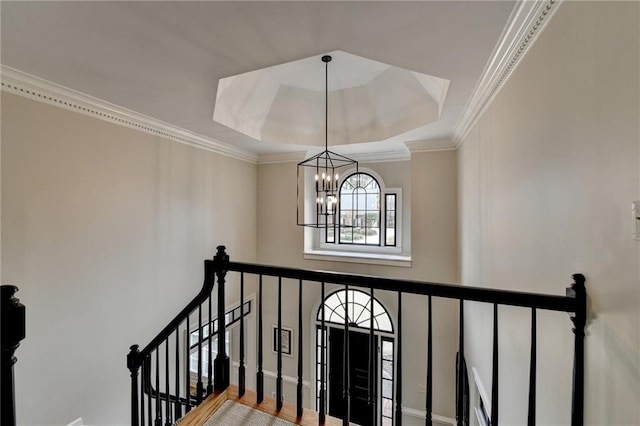 stairs with a chandelier, ornamental molding, and a raised ceiling
