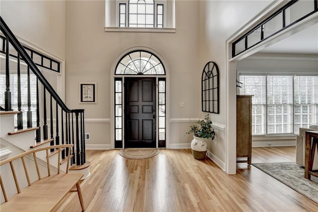 foyer entrance featuring a towering ceiling, healthy amount of natural light, wood finished floors, and stairway