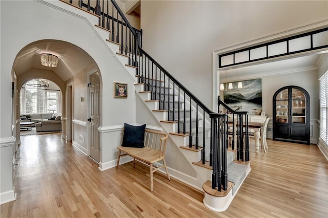 foyer entrance featuring arched walkways, wood finished floors, stairs, a high ceiling, and crown molding