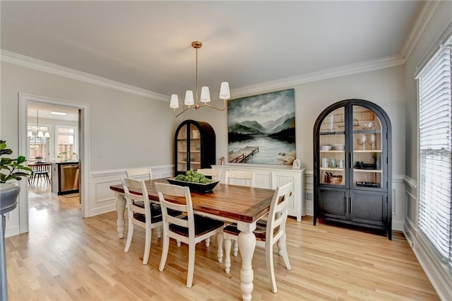 dining space with a chandelier, healthy amount of natural light, ornamental molding, light wood-style floors, and a wainscoted wall