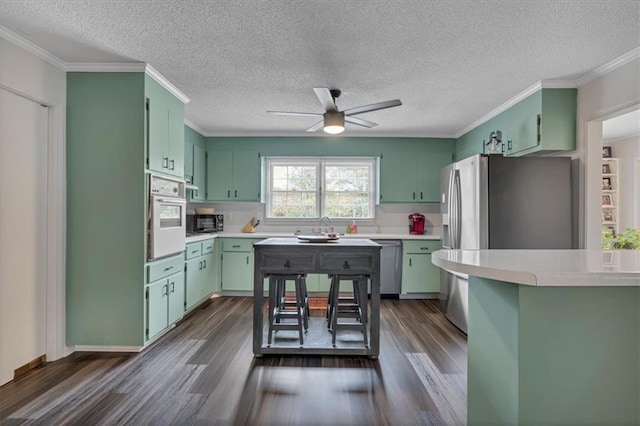 kitchen with ceiling fan, stainless steel appliances, green cabinetry, and dark hardwood / wood-style floors