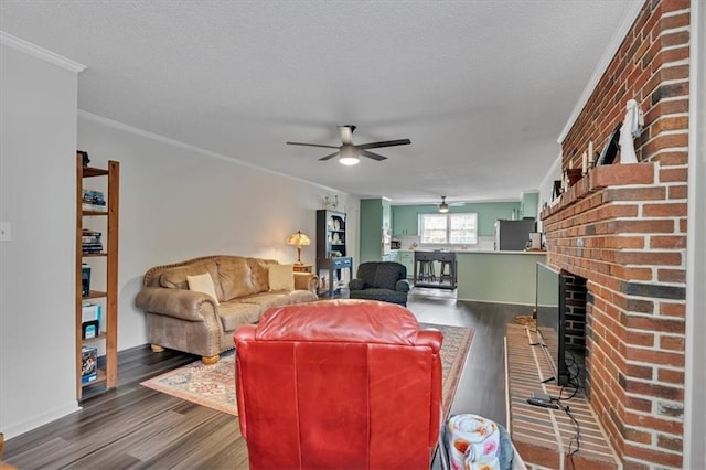 living room with wood-type flooring, a textured ceiling, a brick fireplace, ceiling fan, and ornamental molding