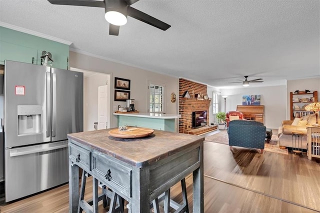 kitchen with a kitchen island, stainless steel refrigerator with ice dispenser, crown molding, a fireplace, and light hardwood / wood-style floors