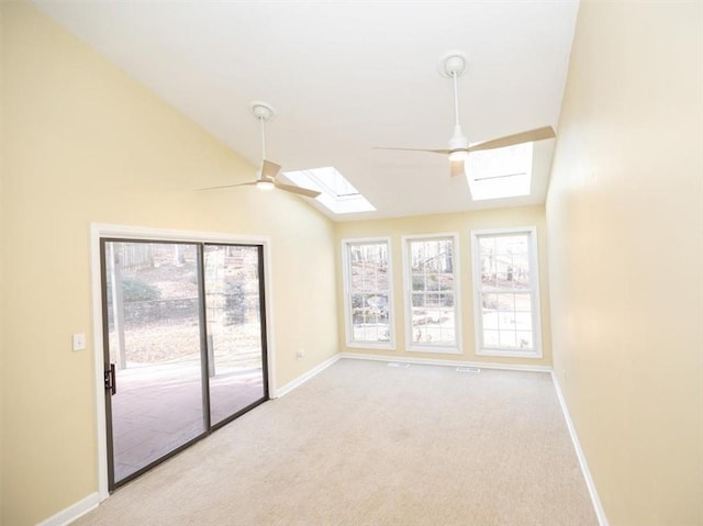 carpeted spare room featuring lofted ceiling with skylight and ceiling fan