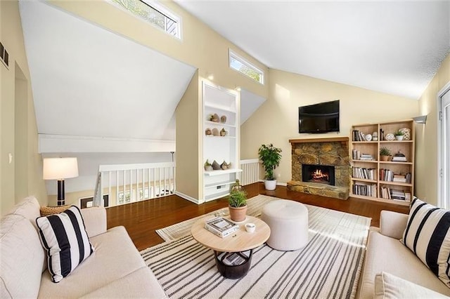 living room featuring lofted ceiling, wood-type flooring, a stone fireplace, and a wealth of natural light