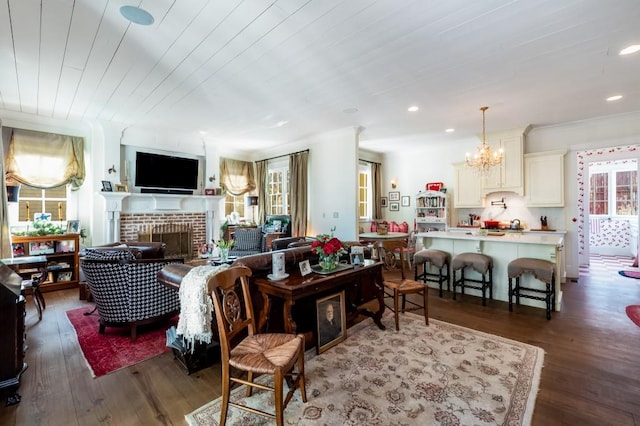 living room featuring dark wood-type flooring, an inviting chandelier, and a brick fireplace